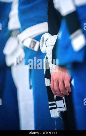 Vue d'artistes martiaux debout dans une rangée portant des uniformes bleus et des ceintures blanches avec un accent sur un nœud noué et une main. Banque D'Images