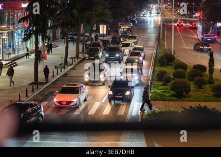 Batumi, géorgie 21 avril 2026 : voitures, autobus et piétons se déplaçant le long d'une rue animée de la ville à batumi, géorgie la nuit, avec des feux de véhicule lumineux an Banque D'Images