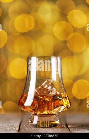 Verre de whisky avec de la glace sur une table en bois et des lumières bokeh dorées en arrière-plan Banque D'Images