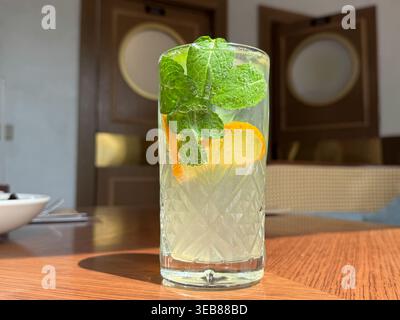 Cocktail rafraîchissant de limonade à la menthe avec des tranches d'orange dans un verre texturé sur une table en bois Banque D'Images
