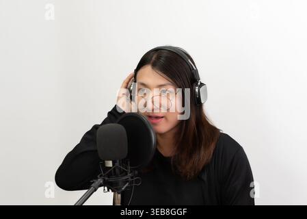 Confiant LGBTQ femme asiatique portant des écouteurs parlant dans le microphone en studio minimal fond moderne créateur de contenu style de vie concentré calme exp Banque D'Images