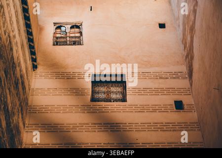 Murs texturés anciens et fenêtres ornées dans une cour marocaine riad.les tons terreux et l'artisanat traditionnel capturent l'âme historique du Maroc Banque D'Images