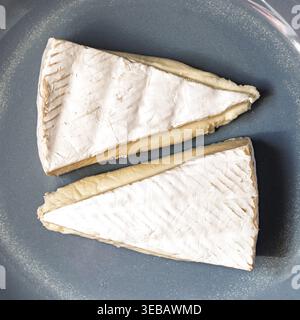 Gros plan de deux quartiers de brie blanc crémeux avec croûte sur une plaque en céramique bleue, mettant en valeur la texture et la délicatesse laitière. Vue de dessus Banque D'Images