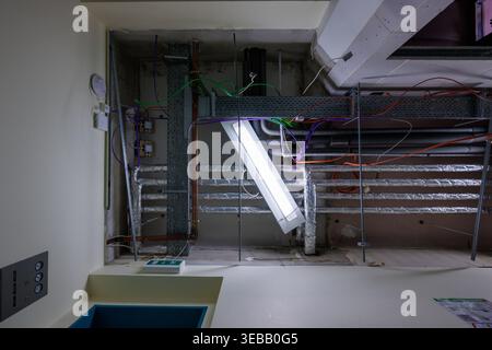 Infrastructure de plafond industriel en construction avec câblage électrique exposé, chemins de câbles, tuyaux de ventilation et lampes fluorescentes suspendues Banque D'Images