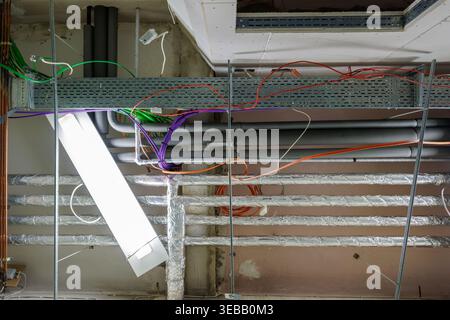 Infrastructure de plafond industriel en construction avec câblage électrique exposé, chemins de câbles, tuyaux de ventilation et lampes fluorescentes suspendues Banque D'Images