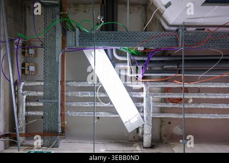Infrastructure de plafond industriel en construction avec câblage électrique exposé, chemins de câbles, tuyaux de ventilation et lampes fluorescentes suspendues Banque D'Images