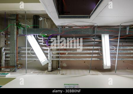 Infrastructure de plafond industriel en construction avec câblage électrique exposé, chemins de câbles, tuyaux de ventilation et lampes fluorescentes suspendues Banque D'Images