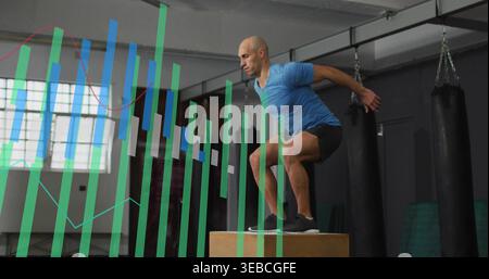 Équilibre homme-top bleu sautant sur la boîte de plyo en bois dans le gymnase avec des sacs, fenêtre, graphiques, espace de copie Banque D'Images