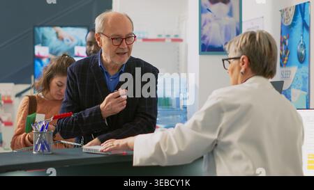 Client senior mettant des boîtes de médicaments sur le comptoir de la pharmacie, achetant des pilules et des suppléments pour le traitement de la récription. Homme prenant des produits pharmaceutiques dans un sac d'achats, caisse enregistreuse. Banque D'Images