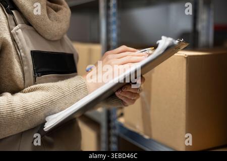 Travailleur logistique dans un dépôt coordonnant le stockage et la manutention des emballages, résolvant les tâches de distribution avant le processus d'expédition. L'intérieur de l'entrepôt comprend des caisses et des étagères pour la chaîne d'approvisionnement. Banque D'Images