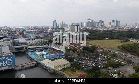Manille, Philippines - 1er mars 2026 : vue aérienne du Manila Ocean Park et du terminal polyvalent de Manille avec les gratte-ciel de la ville sous un ciel brumeux. Banque D'Images
