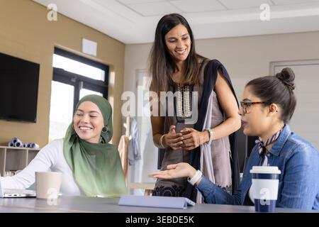 Diverses collègues féminines debout et discutant autour de la table de réunion au bureau avec un ordinateur portable Banque D'Images
