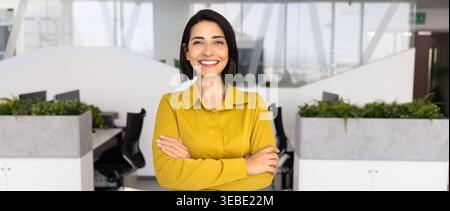 Femme d'affaires latina regardant la caméra debout seul dans le bureau de l'entreprise Banque D'Images