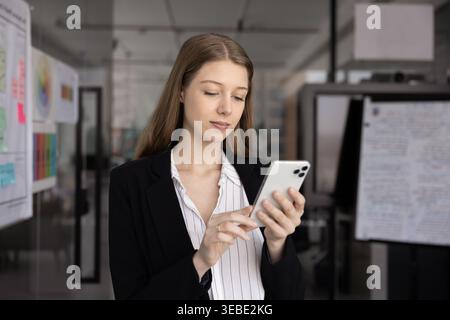 Jeune femme professionnelle debout dans un bureau moderne avec smartphone Banque D'Images