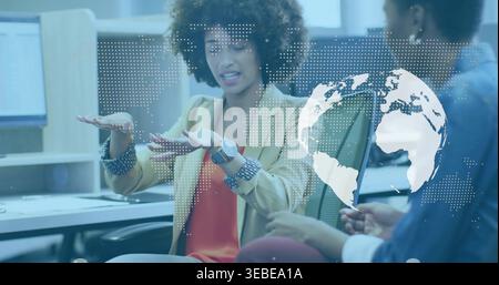 Femme gestuelle en blazer beige sur le dessus orange parlant dans le bureau avec des moniteurs, superposition de carte du monde Banque D'Images