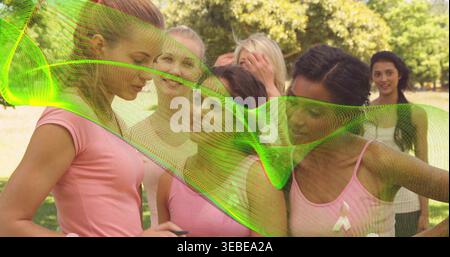 Tenant smartphone, six femmes debout dans le parc ensoleillé portant des hauts roses et ruban, recouvrement vert Banque D'Images