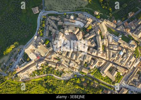 Vue aérienne du centre historique de Montefalco avec sa place circulaire, ses maisons en pierre et ses toits en terre cuite entourés d'oliviers verdoyants Banque D'Images