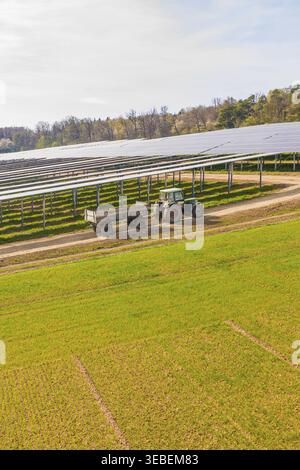 Tracteur avec remorque conduit sur un chemin à côté de grandes rangées de panneaux solaires, Agri PV Bau, Allemagne Banque D'Images