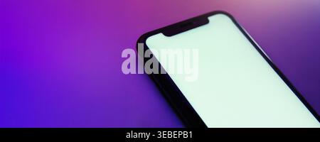 Gros plan d'un téléphone mobile moderne avec un écran blanc vide blanc, éclairé par une lumière rose néon et violette. Maquette de smartphone pour la présentation de la conception d'application avec grand espace pour votre texte. Banque D'Images