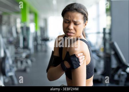 Jeune femme noire grimaçant dans la douleur touchant son épaule dans la salle de gym Banque D'Images