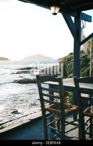 Chaises et tables vides dans un restaurant côtier avec vue sur la mer et l'île lointaine pendant l'heure dorée Banque D'Images