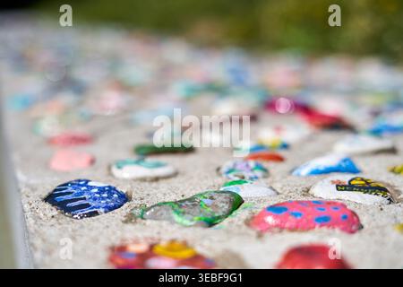Une vue rapprochée de pierres et galets peints de couleurs vives incrustés dans une surface en béton ou en sable, créant une mosaïque décorative vibrante. Les pierres Banque D'Images