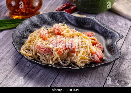 Une délicieuse assiette de spaghettis crémeux avec des morceaux de saumon et du parmesan. Le plat est présenté sur un fond en bois gris rustique avec I frais Banque D'Images