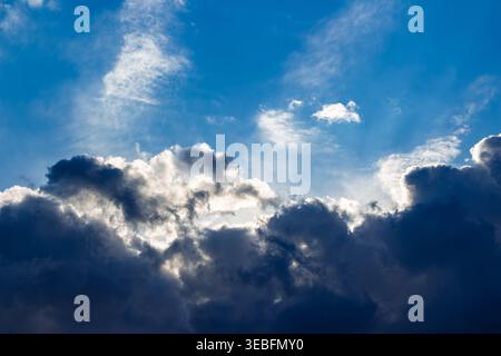 Des rayons de soleil spectaculaires traversent de lourds nuages d'orage sombres contre un ciel Azur vibrant créant un contraste puissant entre la lumière et l'ombre pendant un Banque D'Images