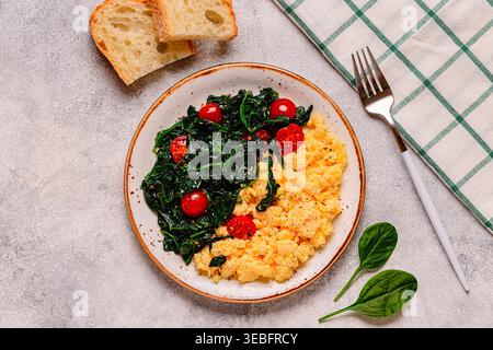 Omelette cuite et épinards avec tomates sur fond clair, vue de dessus. Banque D'Images