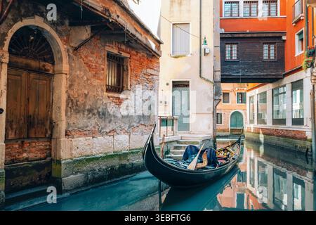 Canal étroit de Venise avec gondole et bâtiments anciens. Ruelle historique intime avec des reflets d'eau calme en Italie. Banque D'Images