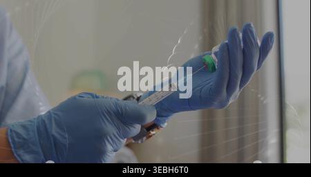 Seringue de préparation, mains gantées en nitrile bleu aspirer le liquide à la clinique, bouchon vert du flacon visible Banque D'Images