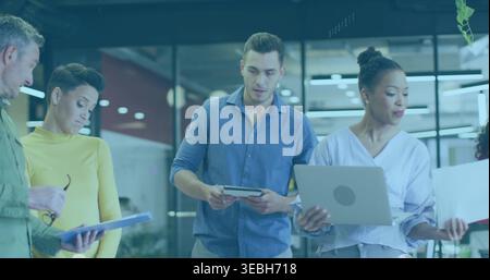 Équipe debout de cinq personnes dans les affaires décontractées tenant des ordinateurs portables, des dossiers, examinant des papiers près du mur de verre Banque D'Images
