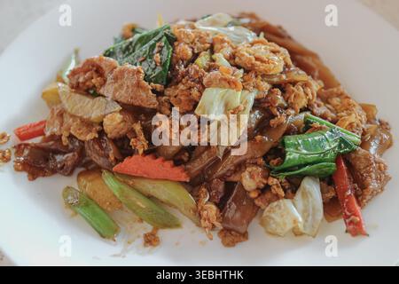 Gros plan sur le bloc, observez des nouilles sautées EW Thai avec œuf de porc et légumes sur une assiette blanche montrant un vrai repas de rue quotidien. Banque D'Images