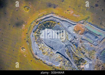 Impact environnemental montrant une érosion sévère du sol, des pistes de machines et des bassins de boue toxiques dans une carrière industrielle massive contrastant fortement avec le reste de la prairie verte. Banque D'Images