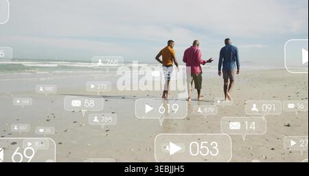 Marcher trois hommes dans des chemises à manches longues et des shorts le long du rivage, tenant le téléphone au milieu des icônes sociales Banque D'Images