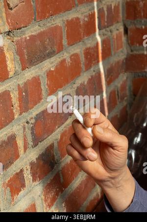 Main tenant la cigarette allumée contre le mur de briques, habitude de fumer gros plan Banque D'Images