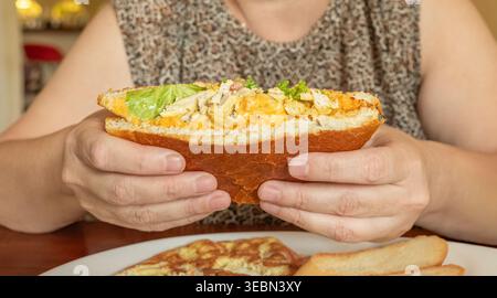 Gros plan photo de mains féminines tenant un demi-sandwich avec du poulet et du fromage. La personne est assise à la table prenant le petit déjeuner avec sandwich grillé. S Banque D'Images