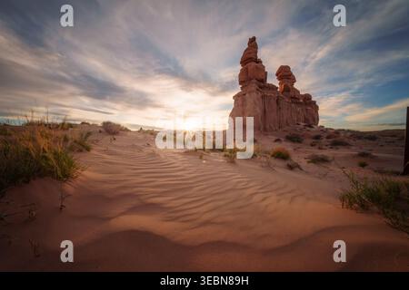 Vue sur la lumière chaude du soleil embrasse les formations rocheuses rouges surréalistes et ondulantes et les dunes de sable sous un ciel peint, Green River, Utah, États-Unis. Banque D'Images