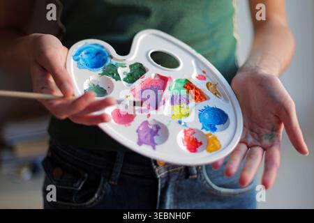Artiste tenant une palette de peinture colorée. Gros plan de mains tenant une palette de peinture avec des couleurs vives et un pinceau, montrant la créativité, l'art et la peinture Banque D'Images