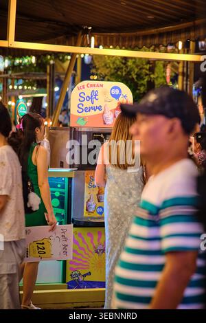 BANGKOK, THAÏLANDE - 01 mars 2025 : kiosque de crème glacée Soft serve à Bangkok avec femme en robe légère et sac tissé choisissant le dessert le soir. Qu. Élevé Banque D'Images