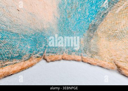 Texture détaillée de matière textile tissée avec un dégradé de bleu vif et des teintes pêche douces, mettant en valeur des fibres complexes et des bords effilochés Banque D'Images