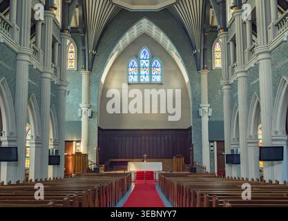 Intérieur de l'église sacrée présentant des plafonds voûtés, des colonnes ornées, des rangées de bancs et un autel proéminent avec une croix Banque D'Images