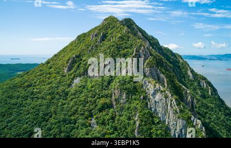 Vue aérienne d'un paysage de montagne verdoyant avec des sommets rocheux surplombant la mer bleue calme et les navires lointains par une journée ensoleillée Banque D'Images