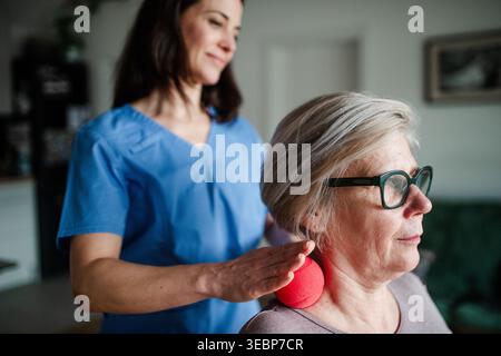 Soignant aidant une femme âgée avec un exercice de rééducation utilisant la boule de massage. Banque D'Images