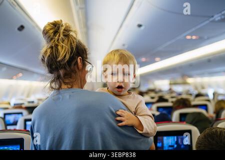 Maman calmant l'enfant bouleversé pendant le vol familial en voyageant dans l'avion. Banque D'Images