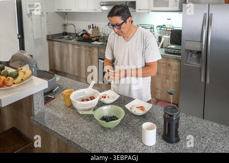 Homme latin préparant un petit déjeuner sain avec des fruits frais et du café dans une cuisine moderne Banque D'Images