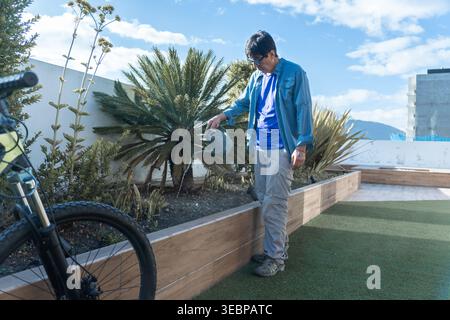 Homme jardinant sur un toit-terrasse, prenant soin des plantes avec un arrosoir sous le ciel bleu Banque D'Images