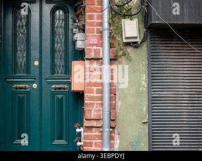 Porte en bois vert classique avec des détails ornés et des poignées en laiton à côté d'un mur rustique de briques rouges avec des tuyaux utilitaires et un signe numéro vingt Banque D'Images