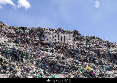 Un site d'enfouissement montre une grande quantité d'ordures empilées haut. La scène est lumineuse avec un ciel bleu clair. Les déchets sont mélangés en piles. Banque D'Images