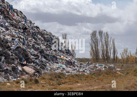 Une décharge dans une zone rurale montre un grand tas d'ordures avec divers déchets et quelques arbres à proximité sous un ciel nuageux pendant l'après-midi. Banque D'Images